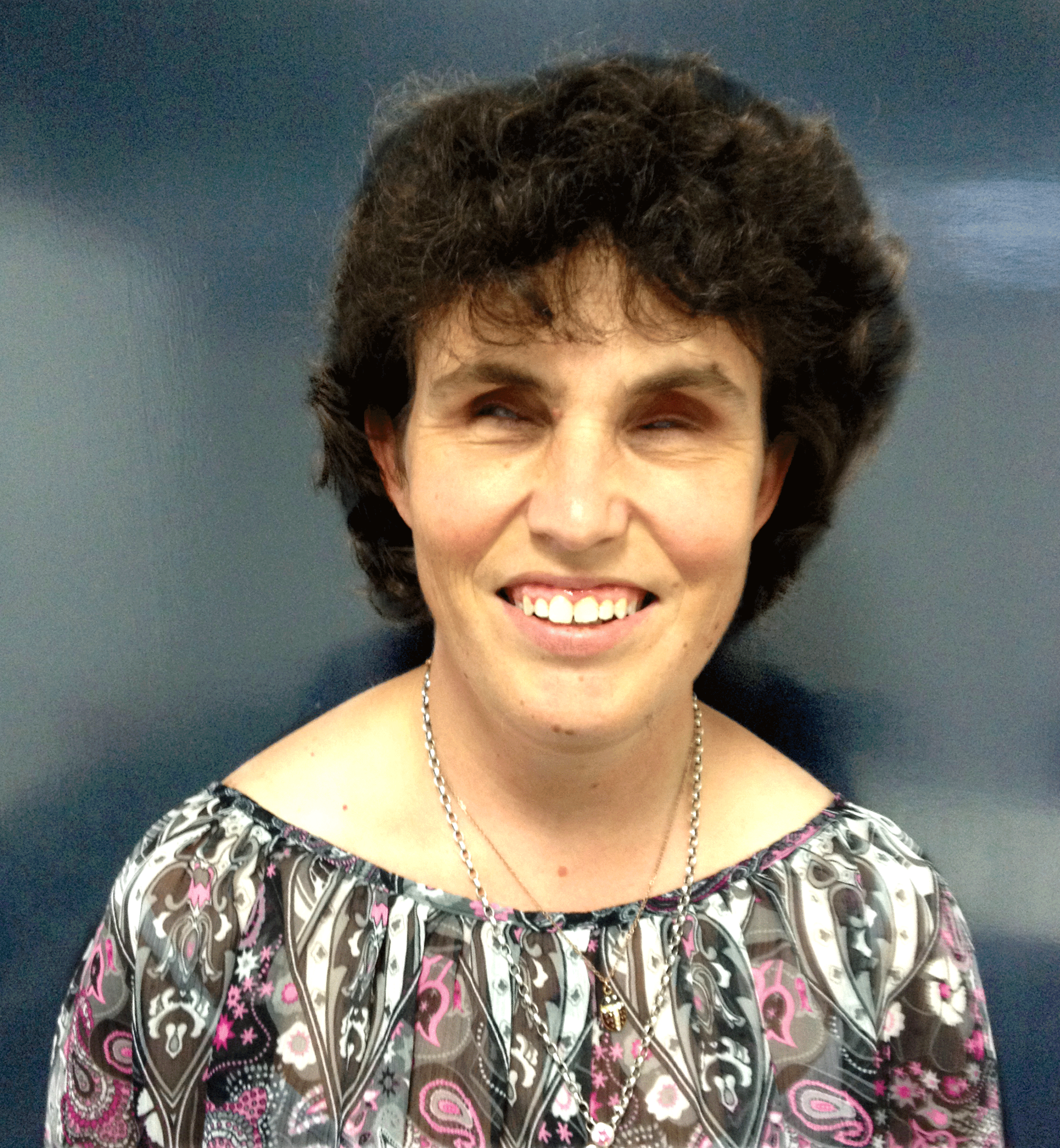 A headshot of a person with short dark curly hair in front of a dark background and smiling at the camera. 